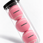 Mockup of three pink tennis balls personalised with VANESSA in green, in a clear tube with a black lid.