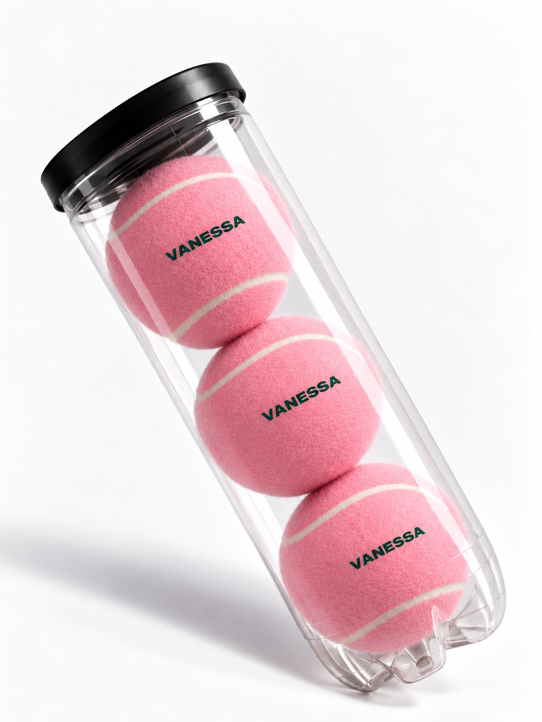 Mockup of three pink tennis balls personalised with VANESSA in green, in a clear tube with a black lid.