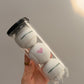 Hand holding a clear Forty-Love can with three white tennis balls: green FORTY-LOVE on the top and bottom balls and a pink heart on the middle ball.