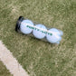 Three white tennis balls in a clear Forty-Love printed can with a black lid, resting beside a white line on a tennis court.
