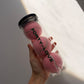 Hand holding three pink tennis balls in a clear Forty-Love printed can with a black lid, in sunlight against a wall.