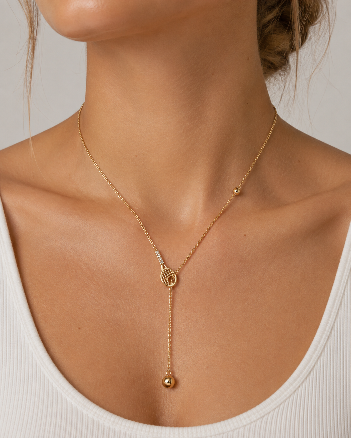 Model wearing a fine gold tennis racquet and ball drop necklace with a white ribbed top | Forty-Love tennis jewellery