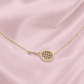 Gold tennis racquet pendant necklace with a pave racquet head, resting on pink satin