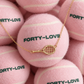 Gold tennis racquet pendant necklace draped over pink Forty-Love tennis balls