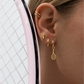Gold tennis racquet charm hoop earring worn with stacked gold hoops against a pink racquet frame