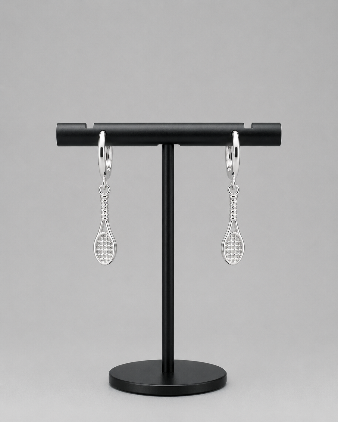 Silver tennis racquet huggie hoop earrings on a black display stand | Forty-Love tennis jewellery
