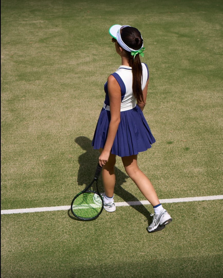 Back view of a women’s tennis dress on court, showing pleated skirt movement and streamlined athletic cut.