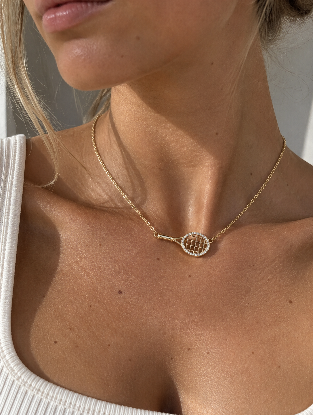 Sideways tennis necklace worn with a gold racquet pendant at the collarbone