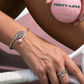 Silver tennis racquet bangle bracelet and racquet ring worn on a hand gripping a racquet, holding a pink Forty-Love tennis ball