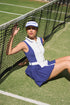Model wearing a white and navy tennis visor on a grass court, premium womens tennis visor for match play.